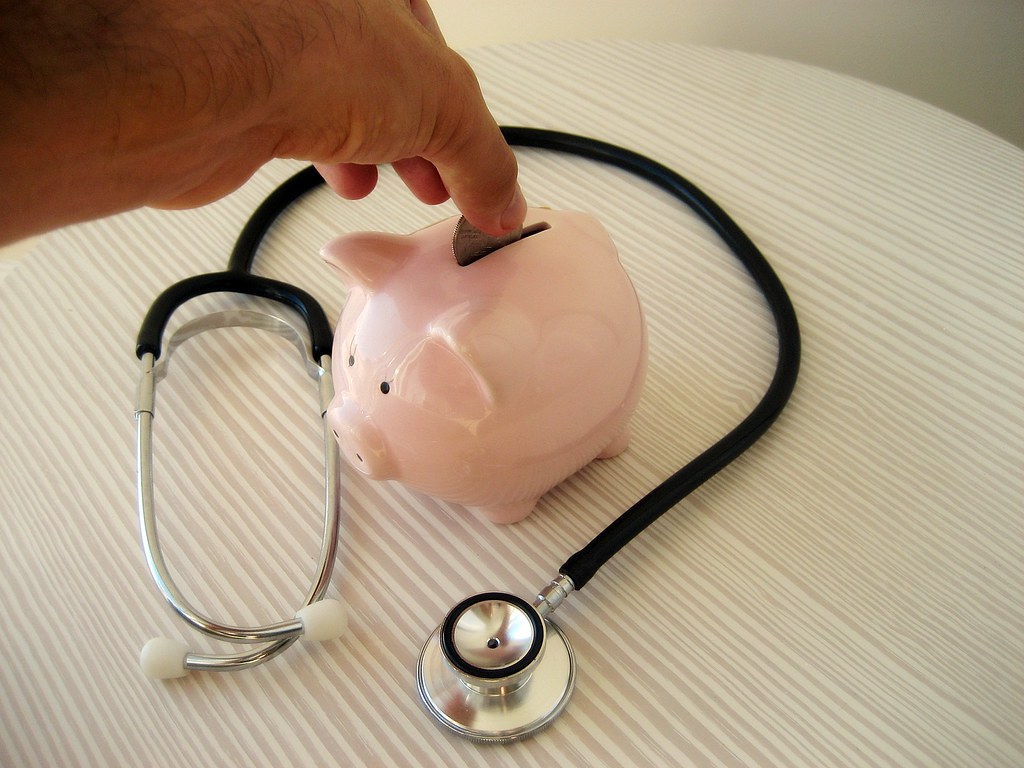 Stethoscope beside a piggy bank, representing FQHC salary vs hospital pay for clinicians