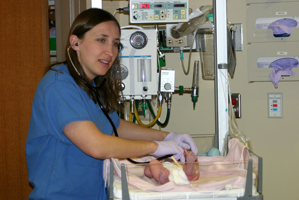Hospital nurse in scrubs checking a newborn with a stethoscope during a shift